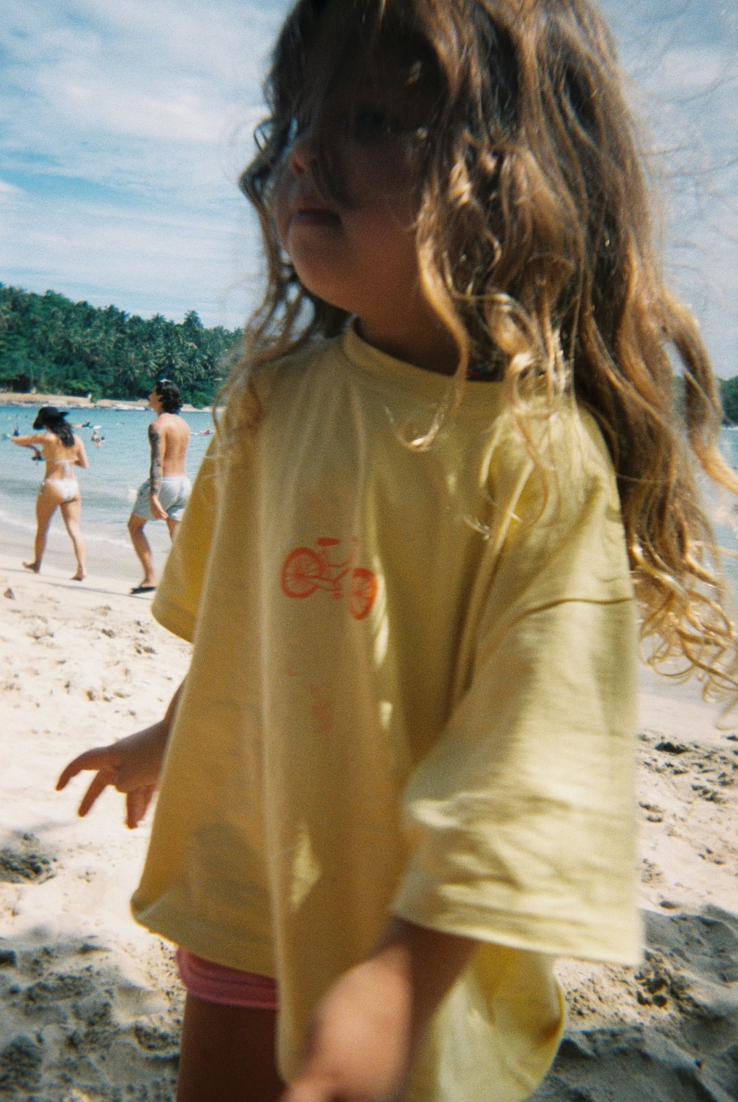 Little girl wearing the oversized Oupah Wheels Feels Tee at the beach
