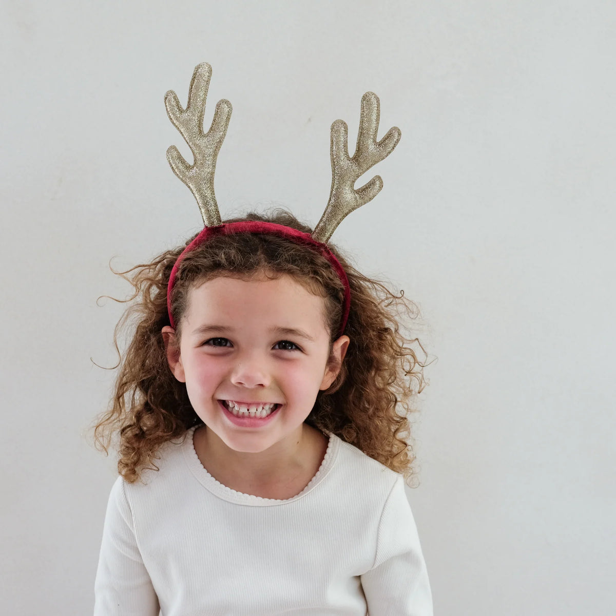 Smiling girl wearing the Mimi & Lulu Rudolph antlers headband