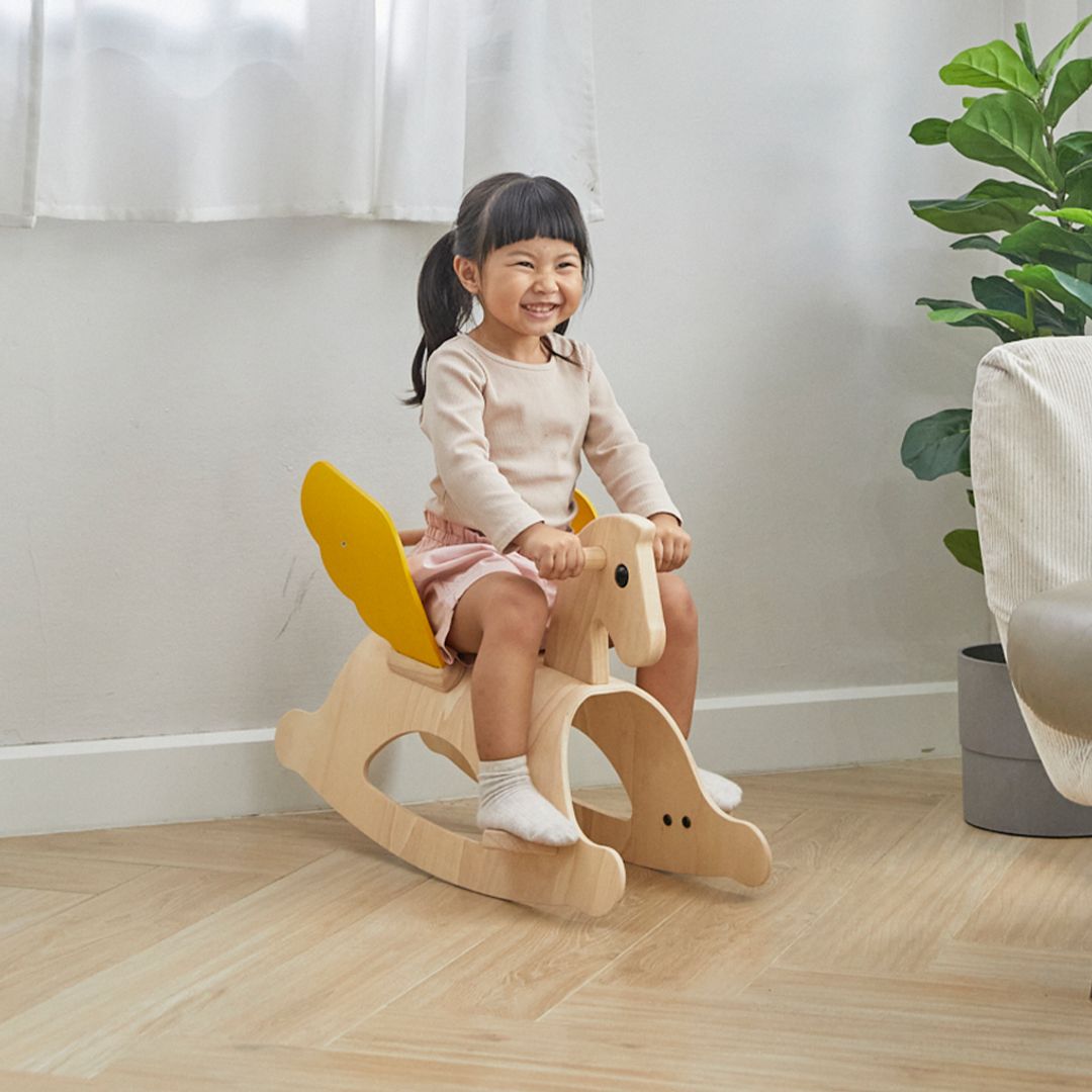 Little girl sitting on the PlanToys Rocking Pegasus in a living room