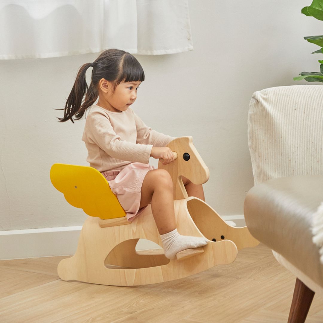 Smiling toddler riding the PlanToys Rocking Pegasus wooden rocking horse