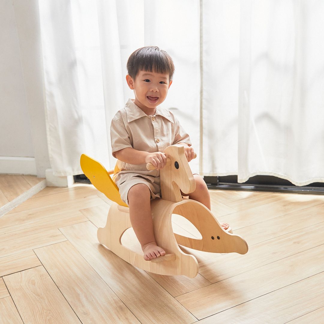 Side view of a toddler riding the PlanToys Rocking Pegasus on a wooden floor