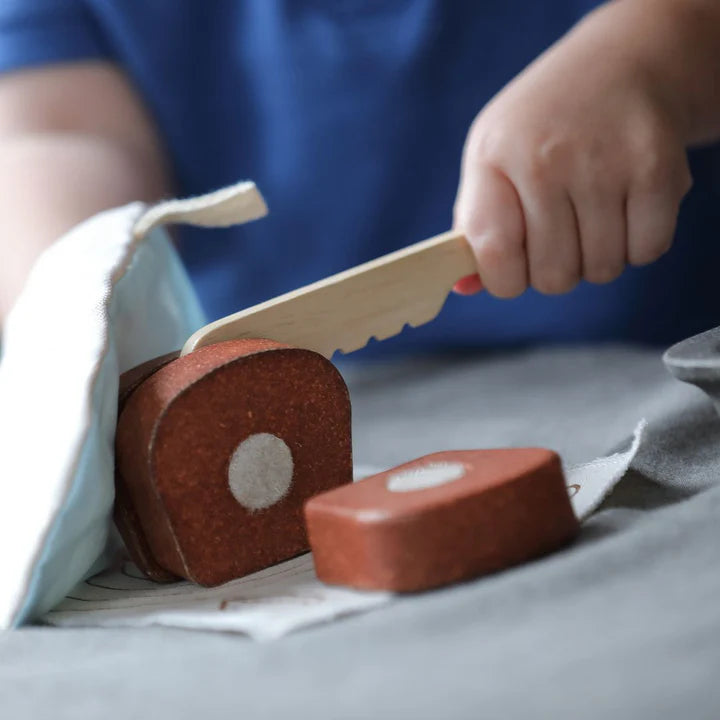 Child slicing the PlanToys wooden bread loaf with a toy knife