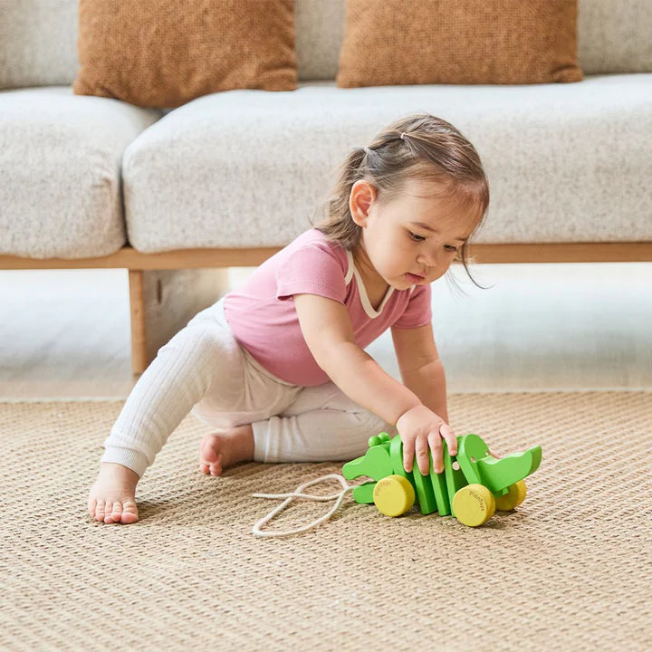 Toddler crawling beside the green PlanToys Dancing Alligator