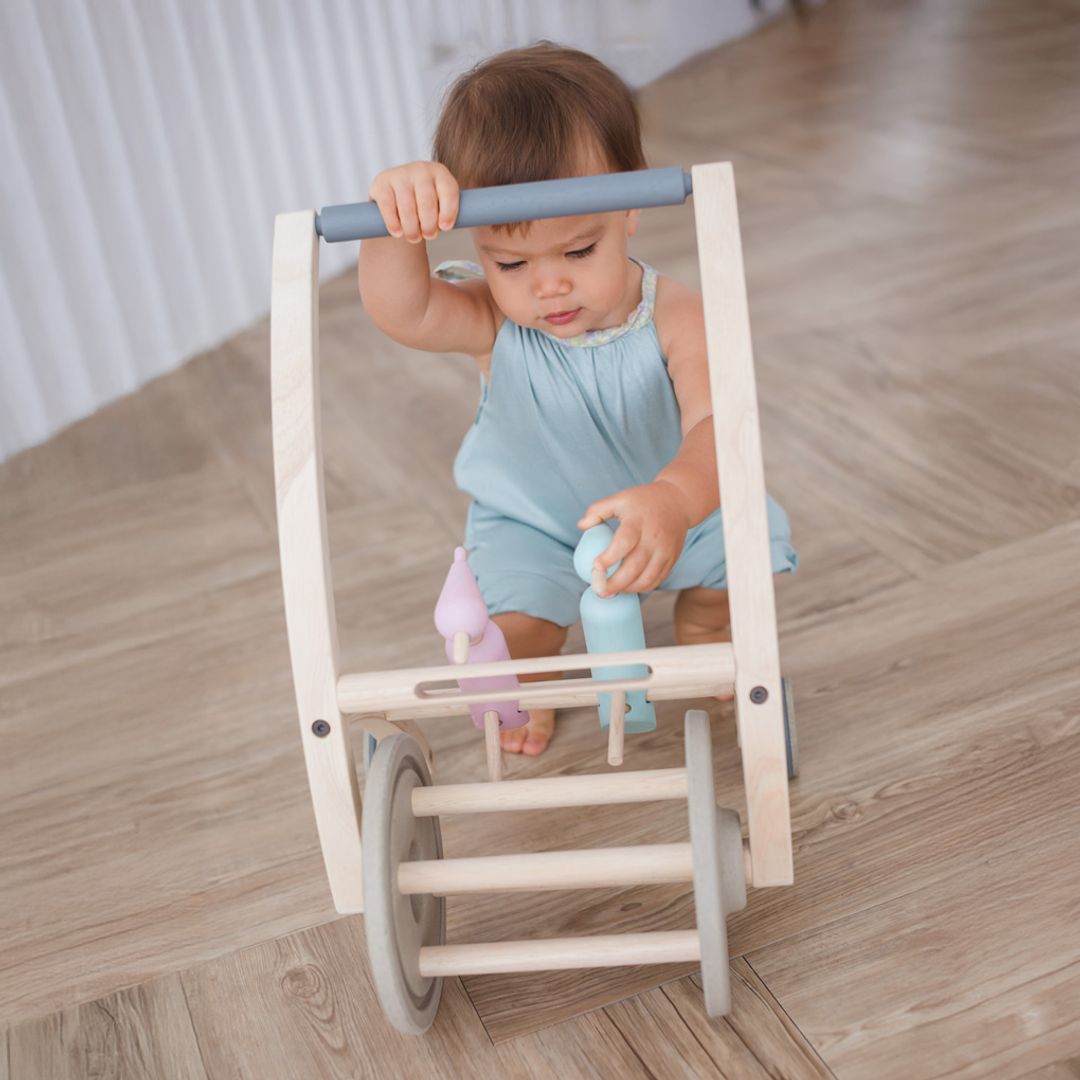 Baby holding the handle of the PlanToys Woodpecker Walker, front view