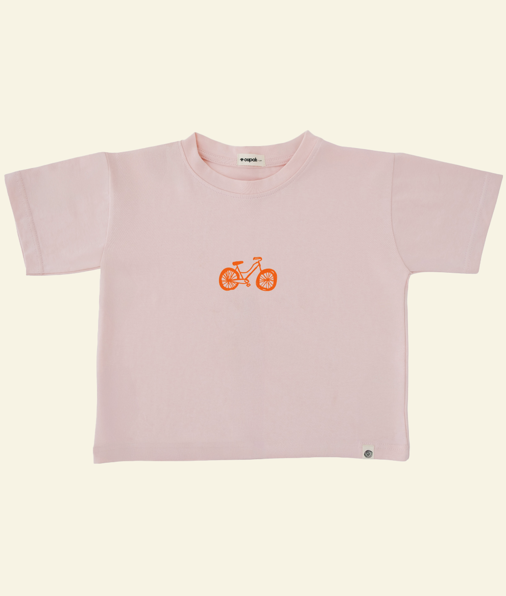 Front of the blush pink Oupah Wheels Feels Tee with small orange wheel