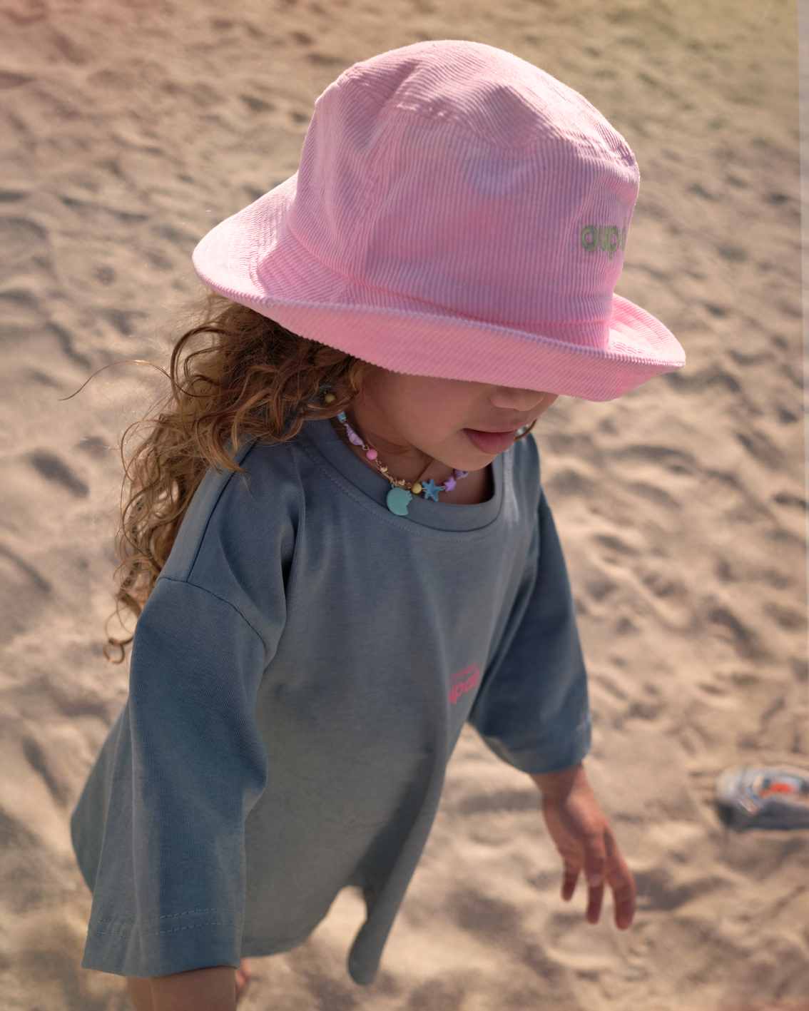 Child on the beach wearing the Peony Pink Oupah Bucket Hattie corduroy hat
