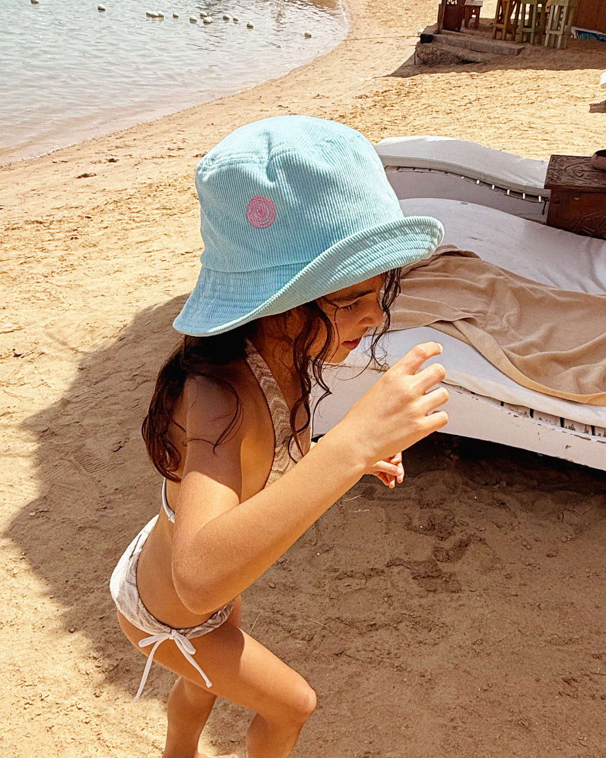 Toddler on the beach wearing the Turquoise Oupah Spiral Bucket Hattie