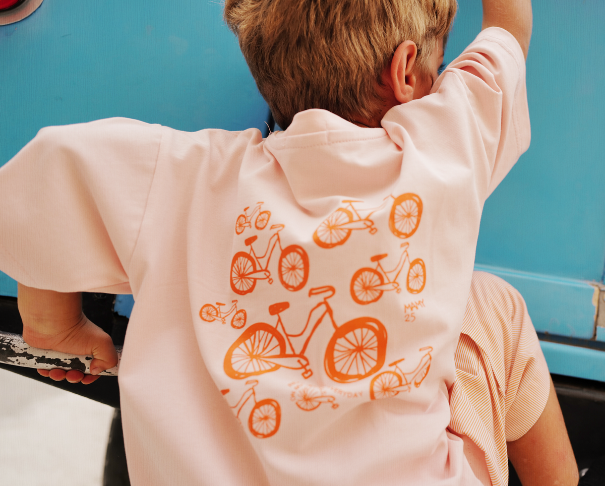 Child by the sea wearing the Oupah Wheels Feels Tee, back view