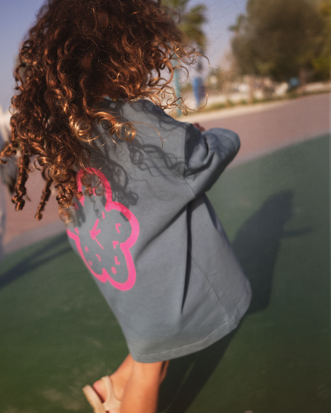 Child wearing the slate blue Oupah Clockwork Tee, showing the pink flower clock print on the back