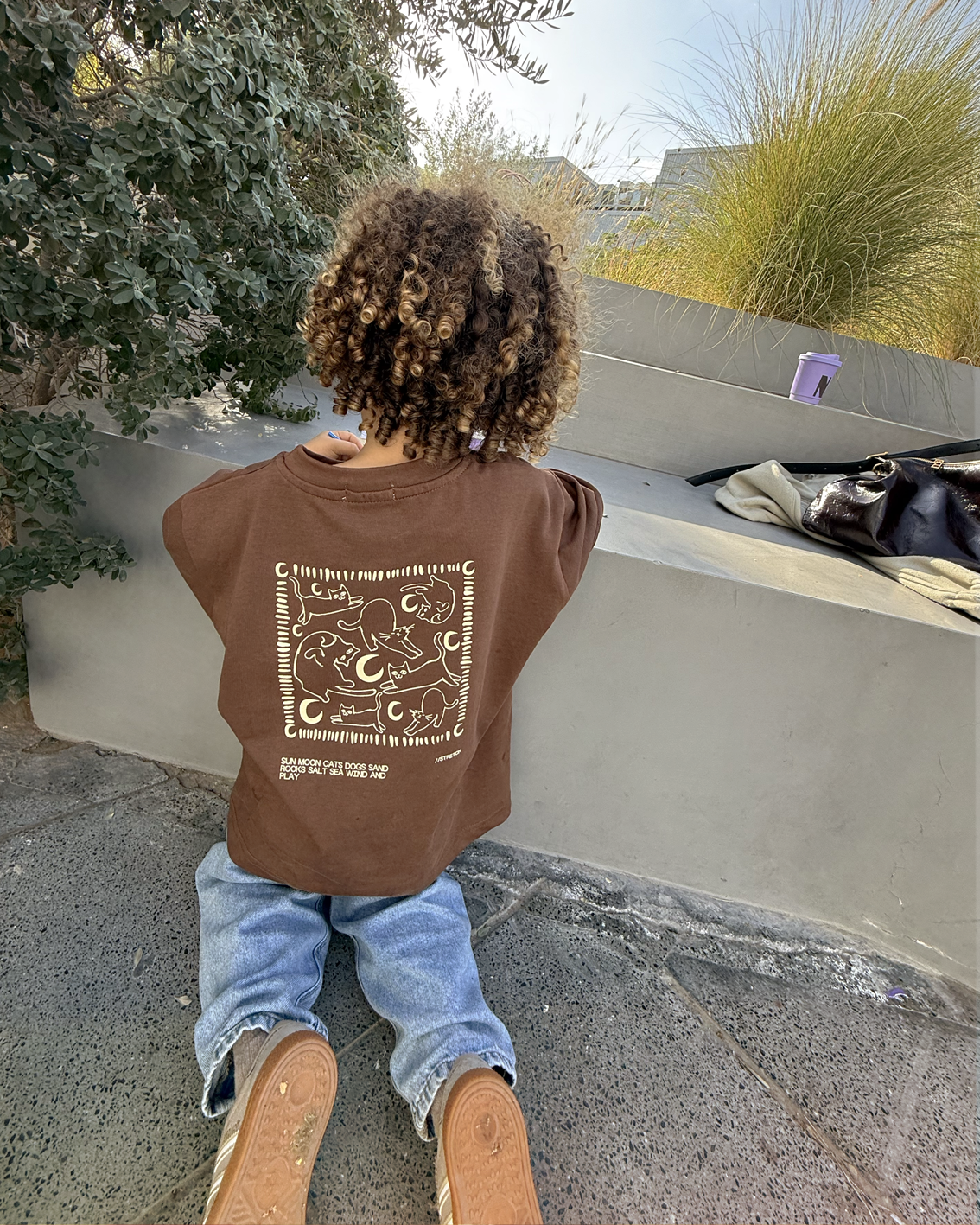 Child wearing the brown Oupah Moon Meow Tee, showing the sun, moon and cats print on the back