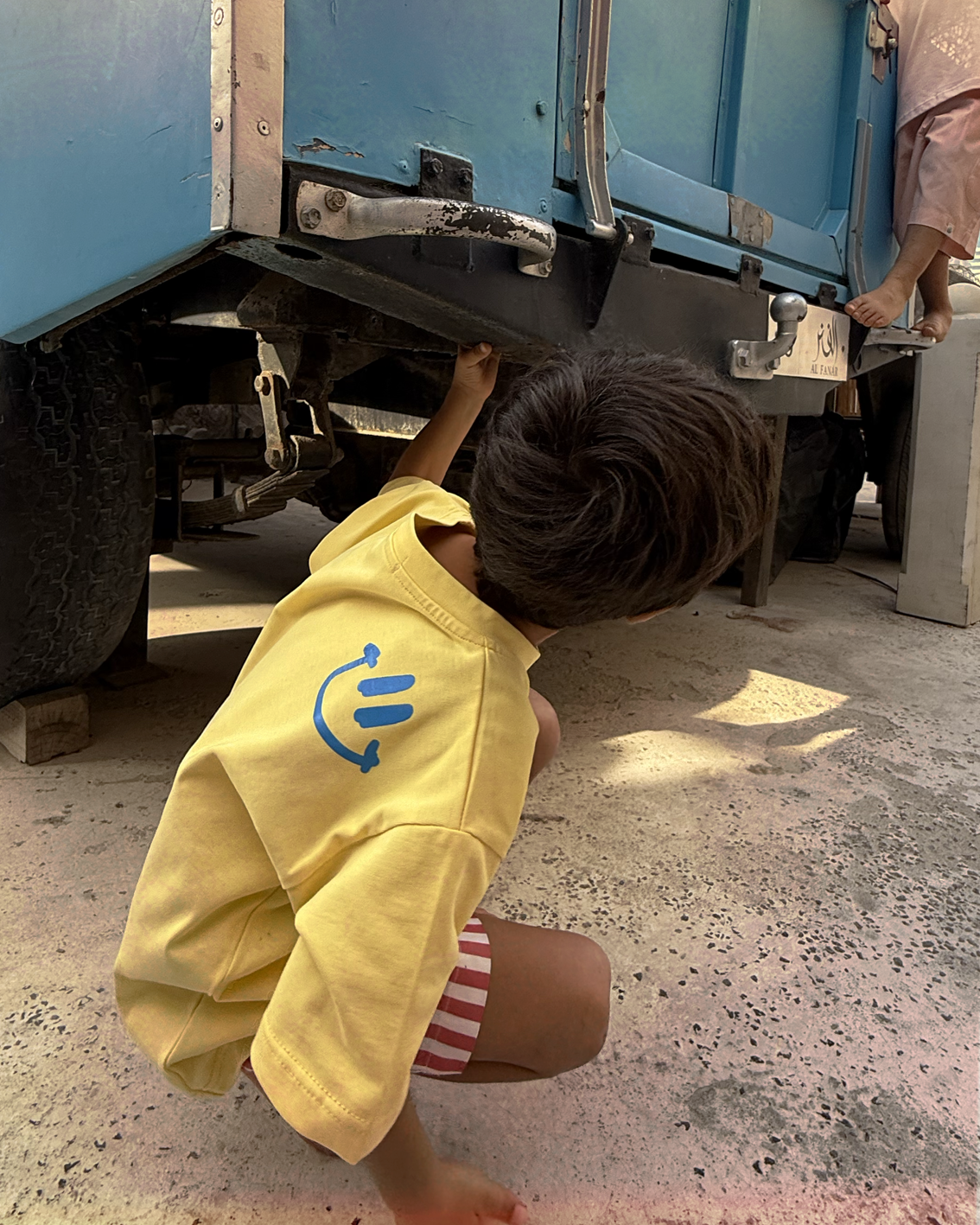 Child crouching in the yellow Oupah Please Tee, showing the blue graphic on the back
