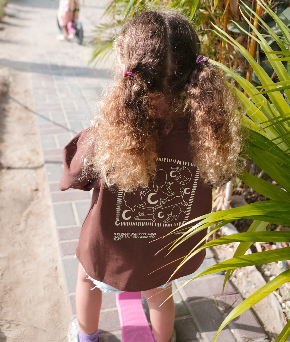 Little girl wearing the brown Oupah Moon Meow Tee outdoors
